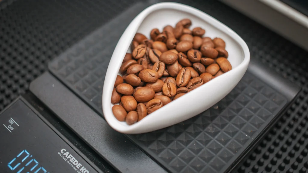 How much coffee per cup shown on a scale with a level tablespoon, a coffee scoop, and a 6 oz cup of ground coffee